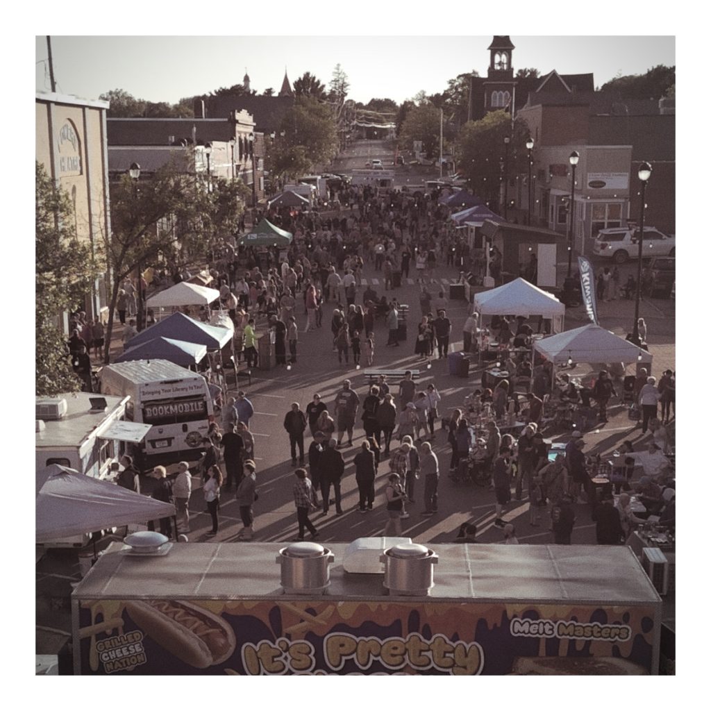 Aerial view of a crowded street during the 'Thursdays on Sweden Street' event, featuring numerous tents, food trucks, and people enjoying live music.