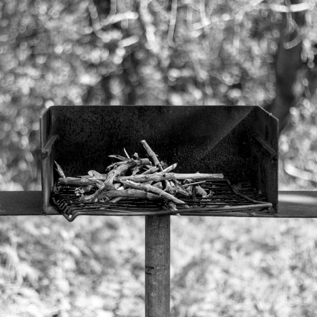 A black and white photo of a small cooking grill mounted on a pole in a small park.