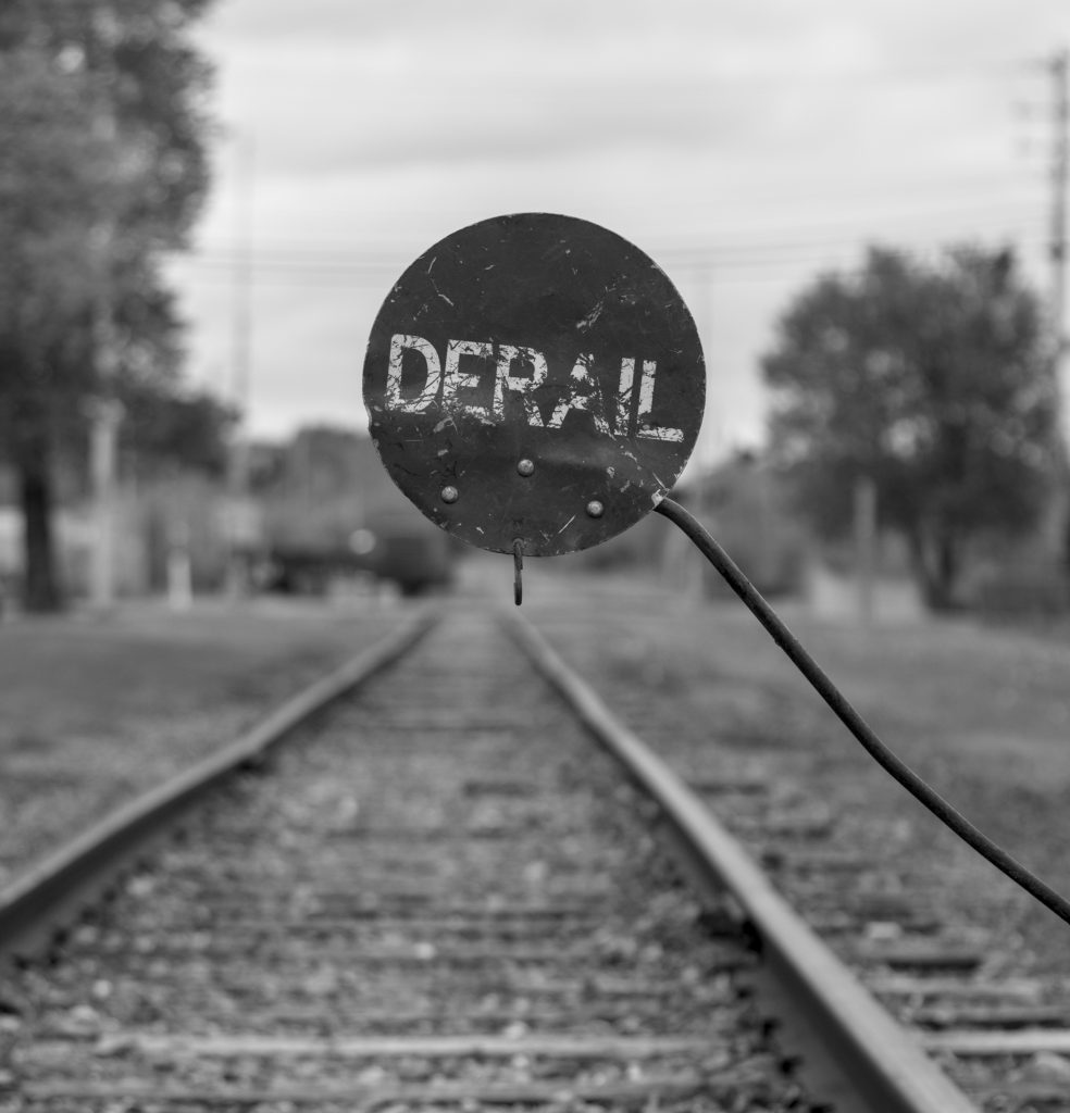 A sign attached to a railroad track says "DERAIL".