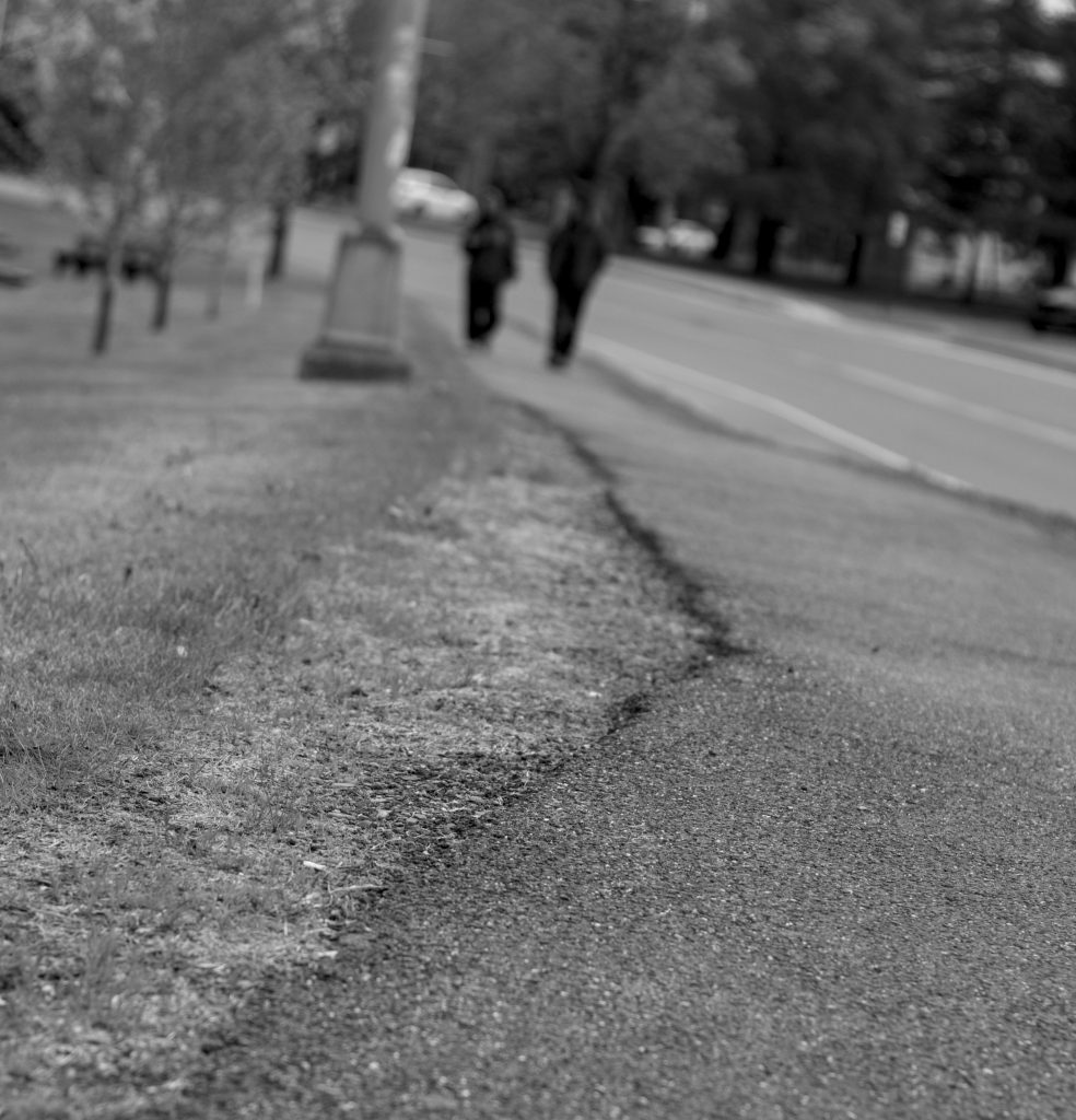 A blurry shot of two people walking along a sidewalk by Riverside Park.