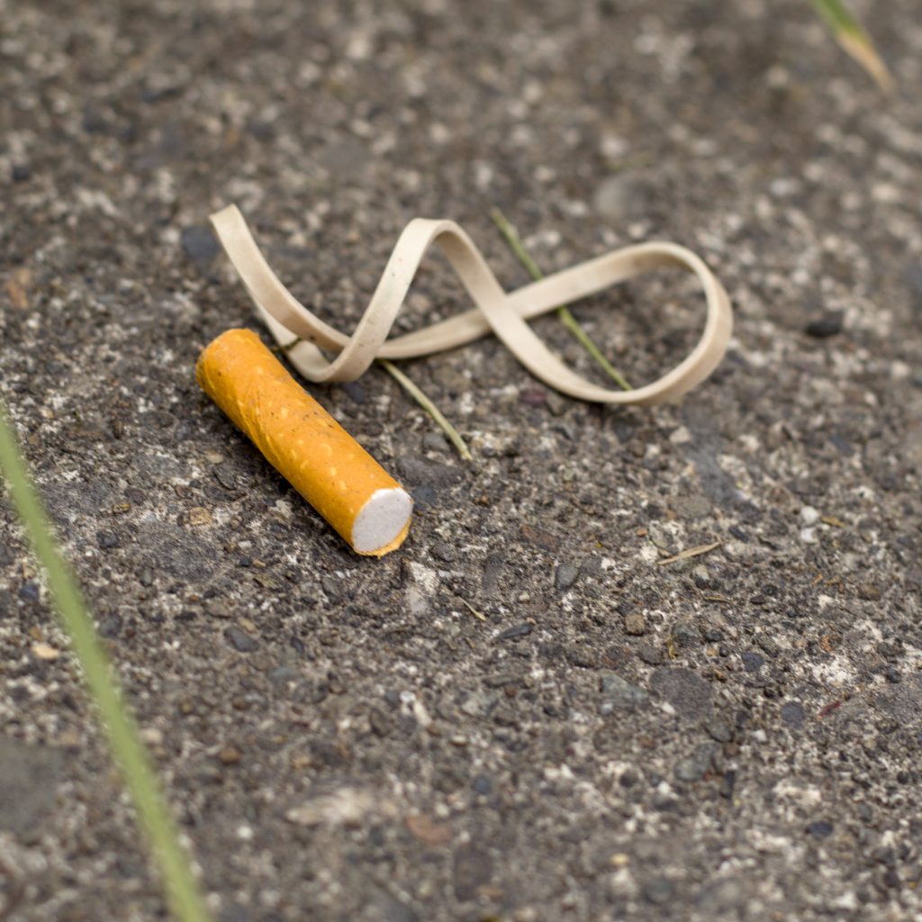 A cigarette filter and rubber band on the pavement.