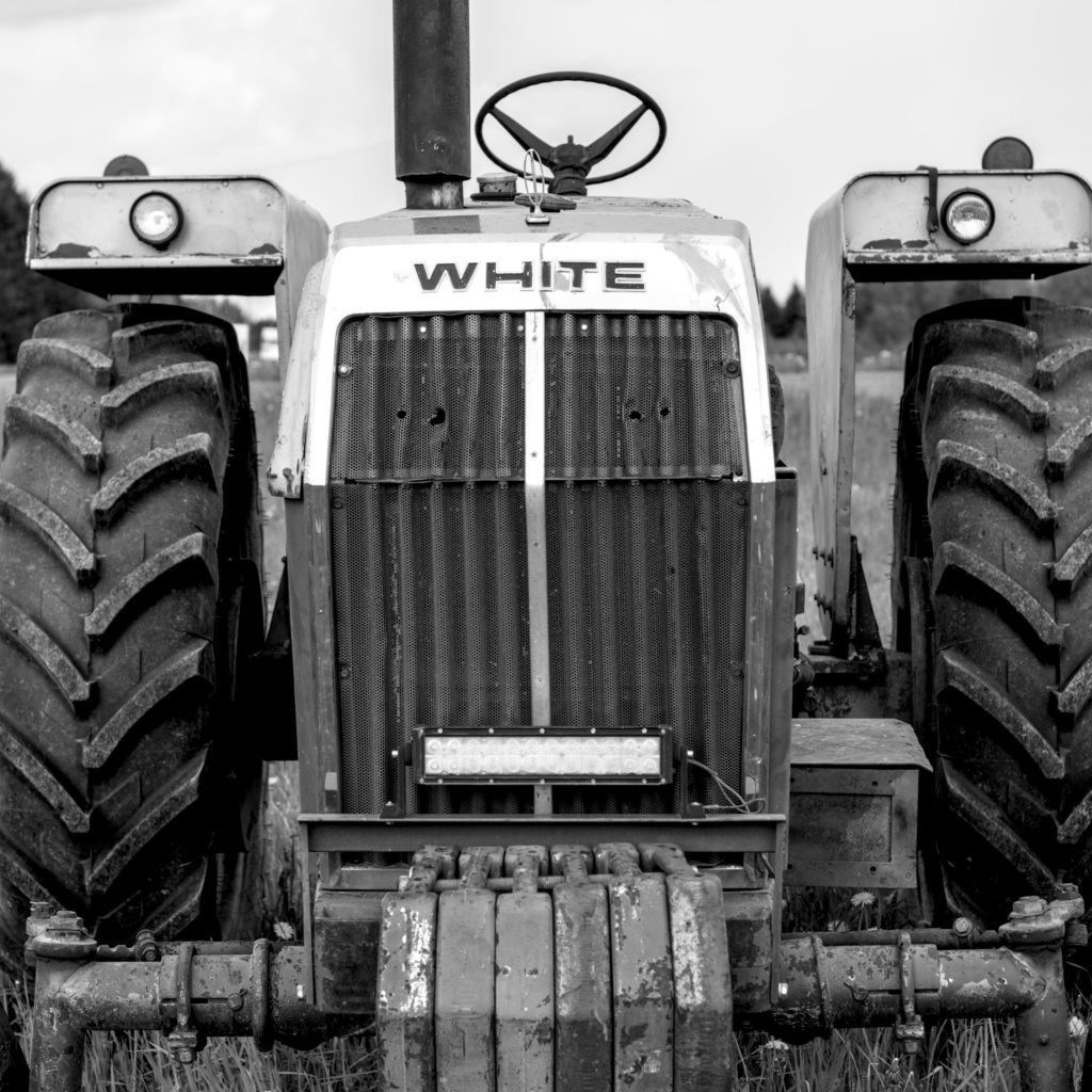 A closeup black and white photo of an old tractor that appears to have bullet holes through the front engine block.